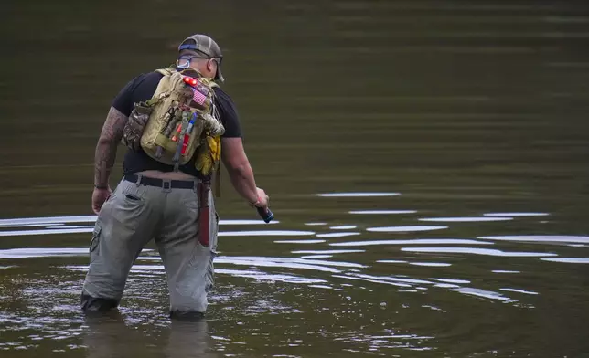 Avi Santos, 23, a civilian from San Antonio, Texas, wades the water at the Guadalupe River as he helps in the recovery effort near Camp Mystic, Sunday, July 6, 2025, in Hunt, Texas, after a flash flood swept through the area. (AP Photo/Julio Cortez)