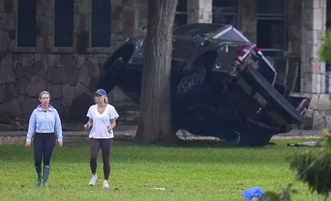 People walk near a vehicle up-ended onto a tree at Camp Mystic along the banks of the Guadalupe River, Sunday, July 6, 2025, in Hunt, Texas, after a flash flood swept through the area. (AP Photo/Julio Cortez)