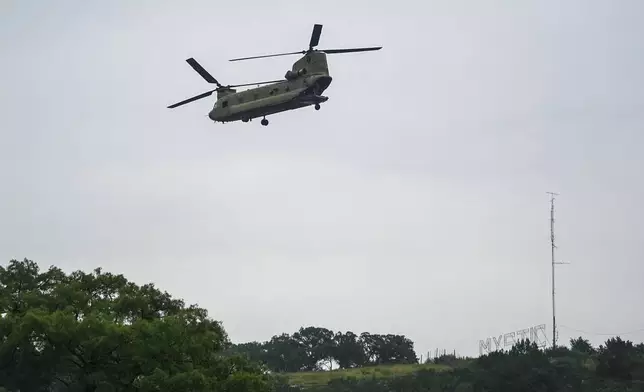 A sign for Camp Mystic is seen on a hill as a heavy-lift military helicopter flies by over the Guadalupe River, Sunday, July 6, 2025, in Hunt, Texas, after a flash flood swept through the area. (AP Photo/Julio Cortez)