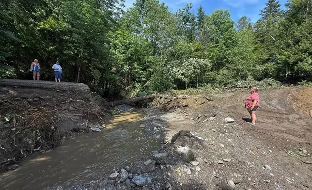 Michelle Tanner, whose yard was washed away by flash flooding, stands in what used to be her driveway as she talks with neighbors on a destroyed roadway, Friday, July 11, 2025 in Sutton, Vt. (AP Photo/Amanda Swinhart)