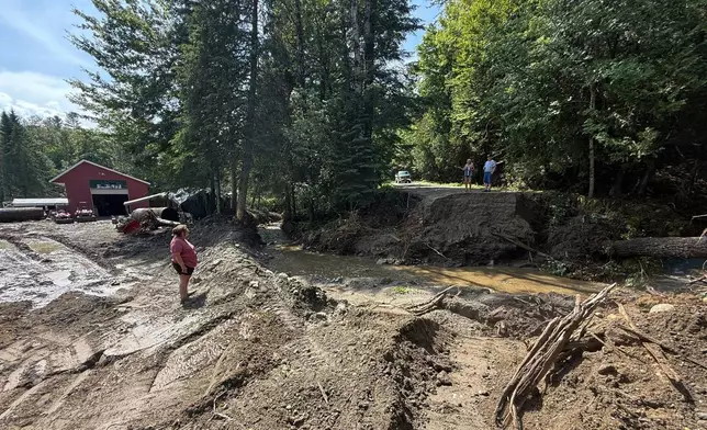 Michelle Tanner, whose yard was washed away by flash flooding, stands in what used to be her driveway as she talks with neighbors on a destroyed roadway, Friday, July 11, 2025 in Sutton, Vt. (AP Photo/Amanda Swinhart)