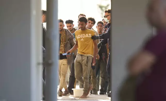 A police officer does a body check to one of migrants rescued south of Crete on their arrival at the the port of Lavrio, Greece, on Thursday, July 10, 2025. (AP Photo/Petros Giannakouris)
