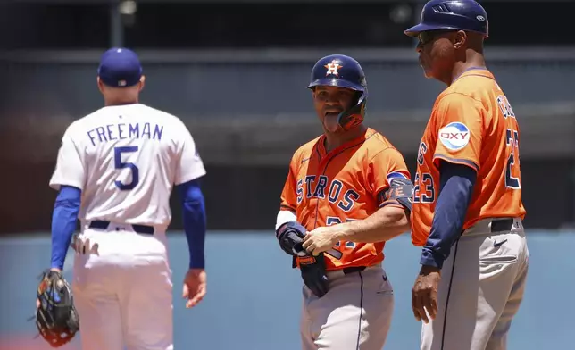 Houston Astros' Jose Altuve, center, reacts after hitting a single as first base coach Dave Clark, right, looks on and Los Angeles Dodgers first baseman Freddie Freeman (5) walks away during the first inning of a baseball game, Sunday, July 6, 2025, in Los Angeles. (AP Photo/Jessie Alcheh)