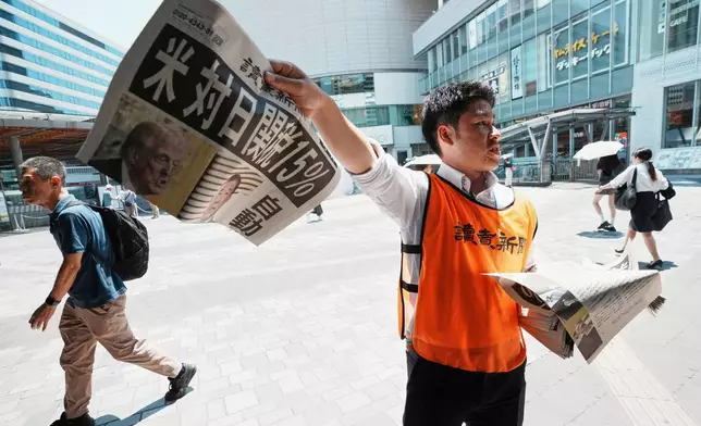 A staff member distributes an extra edition of the Yomiuri Shimbun newspaper reporting that President Donald Trump announced a trade framework with Japan on Tuesday, Wednesday, July 23, 2025, in Tokyo. The headline reads "U.S., a 15% tax on goods imported from Japan." (AP Photo/Eugene Hoshiko)