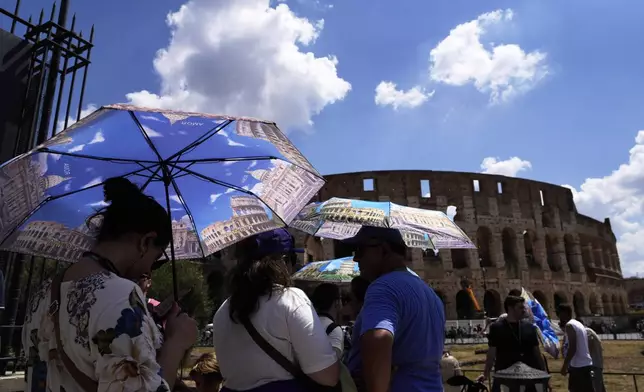 Tourists use umbrellas to shelter from the heat as they line up for a tour of the Forum in Rome, on Tuesday, July 22, 2025. (AP Photo/Gregorio Borgia)