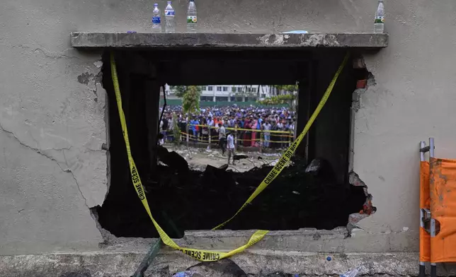 Onlookers are seen through a burnt classroom window of a school building after a Bangladesh air force training jet crashed into it Monday in Dhaka, Bangladesh, Tuesday, July 22, 2025. (AP Photo/Mahmud Hossain Opu)