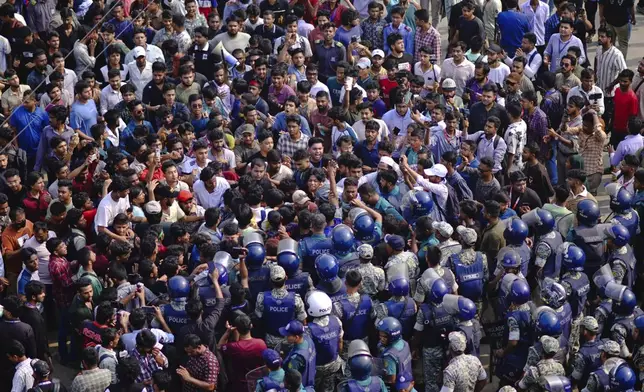 Police officers stand guard as students shout slogans during a protest near the site of the crash of a Bangladesh air force training jet into a school, demanding accountability, compensation for victims' families and the halt of training flights, in Dhaka, Bangladesh, Tuesday, July 22, 2025. (AP Photo/Mahmud Hossain Opu)