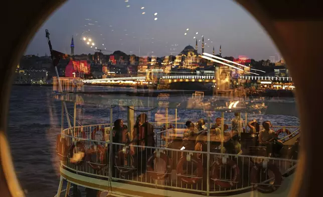 With the Suleymaniye Mosque in the background, passengers, seen through a window, board a ferry before departing from the Karakoy terminal in Istanbul, Turkey, Friday, June 13, 2025. (AP Photo/Francisco Seco)