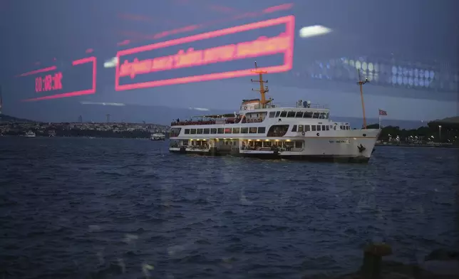 A ferry, seen through a window, sails along the Bosphorus bound for the Karakoy terminal in Istanbul, Turkey, Friday, June 13, 2025. (AP Photo/Francisco Seco)
