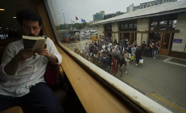 A passenger reads a book as others board a ferry at the Eminonu terminal on the Golden Horn in Istanbul, Turkey, Sunday, May 25, 2025. (AP Photo/Francisco Seco)
