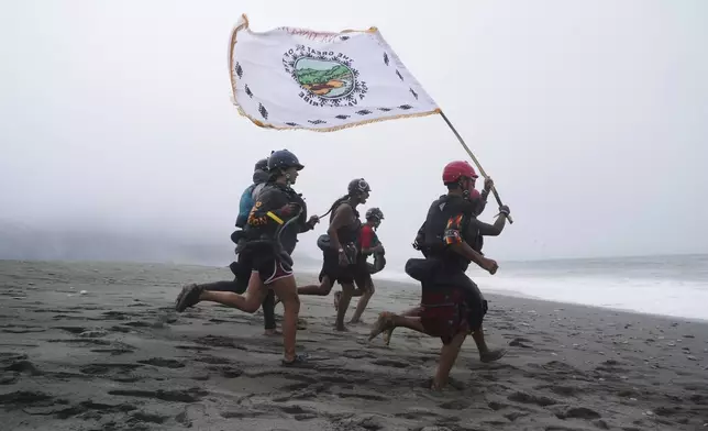 Youth from the Hoopa Valley Tribe run with a flag across a sandy stretch that separates the Klamath River from the Pacific Ocean on Friday, July 11, 2025, in Klamath, Calif. (AP Photo/Brittany Peterson)