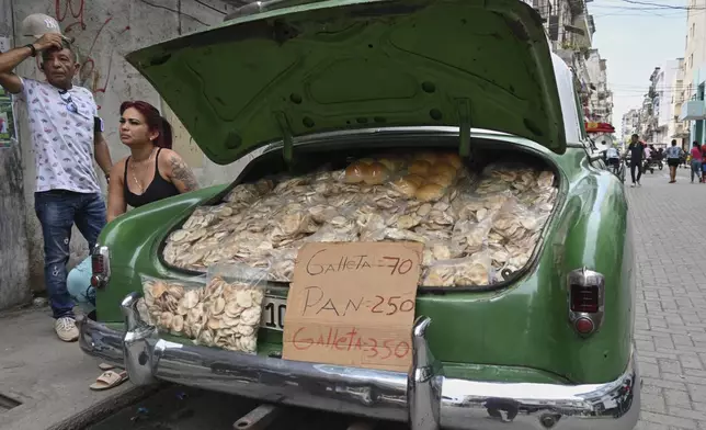 Vendors wait for customers next to the trunk of their American classic car stuffed with homemade crisps and bread, in Havana, Cuba, Tuesday, July 15, 2025. (AP Photo/Jorge Luis Baños)