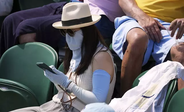 A woman protects her arms and face from the sun as she sits in the crowd to watch the Wimbledon Tennis Championships in London, Monday, June 30, 2025. (AP Photo/Kirsty Wigglesworth)