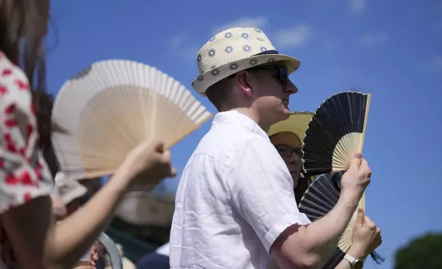 Visitors use fans to stay cool at the Wimbledon Tennis Championships in London, Monday, June 30, 2025. (AP Photo/Kin Cheung)