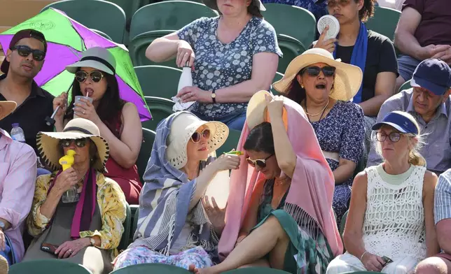 Tennis supporters use fans and water spray to cool during the Wimbledon Tennis Championships in London, Monday, June 30, 2025. (AP Photo/Kirsty Wigglesworth)