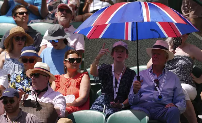 Spectators use an umbrella to protect against the sun during the Wimbledon Tennis Championships in London, Tuesday, July 1, 2025.(AP Photo/Kirsty Wigglesworth)