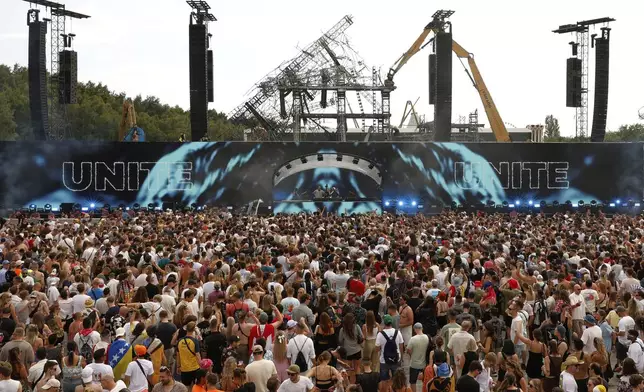 People listen to Odymel B2B and Pegassi performing at the Tomorrowland music festival in Boom, Belgium, Friday, July 18, 2025, two days after a huge fire on Wednesday severely damaged the main stage, rear. (AP Photo/Omar Havana)
