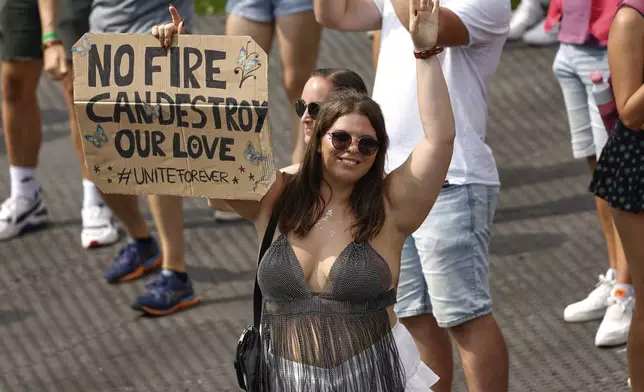 A woman holds a placard as Odymel B2B and Pegassi perform at the Tomorrowland music festival in Boom, Belgium, Friday, July 18, 2025, two days after a huge fire on Wednesday severely damaged the main stage. (AP Photo/Omar Havana)