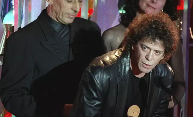 FILE - Lou Reed speaks at the podium, center, as he and his Velvet Underground band mates John Cale, left, and at Martha Morrison are inducted into the Rock and Roll Hall of Fame in New York on s Jan. 17, 1996. (AP Photo/Mark Lennihan, File)