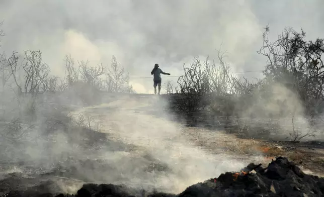 A man speaking on his cellphone walks through a burned area in Souni village, Cyprus, during a massive wildfire on the southern side of the east Mediterranean island nation's Troodos mountain range, Thursday, July 24, 2025. (AP Photo/Petros Karadjias)