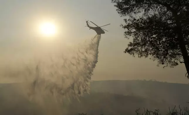 A helicopter drops water over a burned forest in Souni village, Cyprus, during a massive wildfire on the southern side of the east Mediterranean island nation's Troodos mountain range, Thursday, July 24, 2025. (AP Photo/Petros Karadjias)