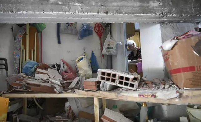 A woman is seen in her apartment after a wall collapsed following a bomb explosion, at the entrance of the home of president of the Greek association of prison guards, at a suburb of Thessaloniki, northern Greece, Saturday, July 26, 2025. (AP Photo/Giannis Papanikos)