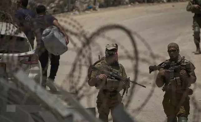 Israeli soldiers stand guard as Syrian Druze people cross back into Syria at the Israeli-Syrian border, in the Israeli-controlled Golan Heights town of Majdal Shams, Thursday, July 17, 2025. (AP Photo/Leo Correa)