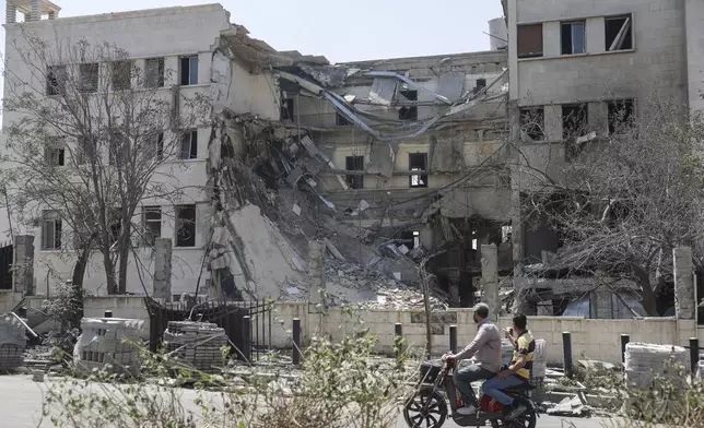 People pass in front the Syrian Defense Ministry building which on Wednesday was heavily damaged by Israeli airstrikes in Damascus, Syria, Thursday, July 17, 2025. (AP Photo/Ghaith Alsayed)