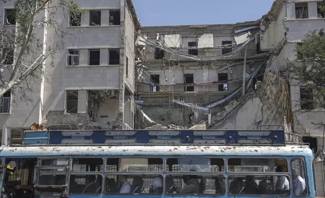 People sit in a bus passing in front the Syrian Defense Ministry building which on Wednesday was heavily damaged by Israeli airstrikes in Damascus, Syria, Thursday, July 17, 2025. (AP Photo/Ghaith Alsayed)