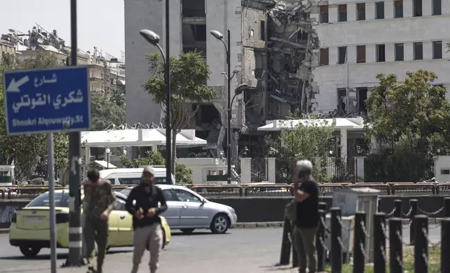 People pass in front the Syrian Defense Ministry building which on Wednesday was heavily damaged by Israeli airstrikes in Damascus, Syria, Thursday, July 17, 2025. (AP Photo/Ghaith Alsayed)
