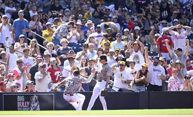 San Diego Padres third baseman Manny Machado (13) is helped up by left fielder Bryce Johnson after making a sliding catch on a popup hit by Philadelphia Phillies' Brandon Marsh during the ninth inning of a baseball game Sunday, July 13, 2025, in San Diego. (AP Photo/Orlando Ramirez)