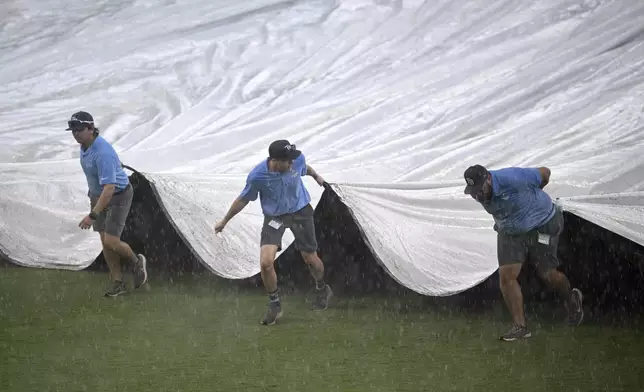 Members of the grounds crew cover the infield during a weather delay in the seventh inning of a baseball game between the Tampa Bay Rays and the Baltimore Orioles, Sunday, July 20, 2025, in Tampa, Fla. (AP Photo/Phelan M. Ebenhack)