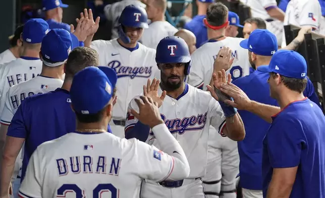 Texas Rangers' Marcus Semien, center front, and Corey Seager, center rear, celebrate with teammates after they scored on an Adolis Garcia single in the third inning of a baseball game against the Atlanta Braves, Saturday, July 26, 2025, in Arlington, Texas. (AP Photo/Tony Gutierrez)