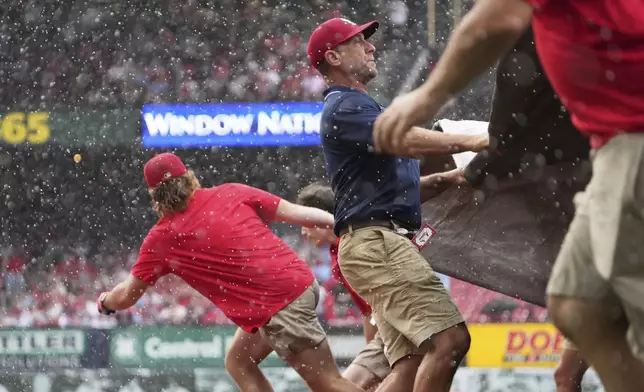 Members of the Busch Stadium grounds crew unfurl a tarp over the field at the start of a rain delay during the third inning of a baseball game between the St. Louis Cardinals and the Atlanta Braves Sunday, July 13, 2025, in St. Louis. (AP Photo/Jeff Roberson)