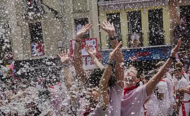 Revellers cool off with water thrown from balconies during the start of nine days of uninterrupted partying in Pamplona's famed running-of-the-bulls festival in Pamplona, Spain, Sunday, July 6, 2025. (AP Photo/Miguel Oses)