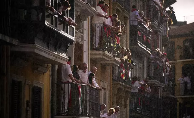 Attendees wait on their balconies as rain begins to fall during the first day of the running of the bulls, at the San Fermín fiestas in Pamplona, Spain, Monday, July 7, 2025. (AP Photo/Miguel Oses)
