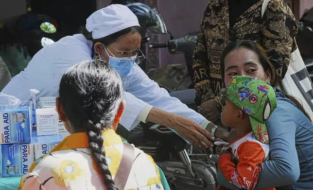 A child is helped by a medical official for a check up while villagers take refuge in Buddhist pagoda in Srey Snam district, Siem Reap province, Cambodia, Sunday, July 28, 2025, amid the fighting between Thailand and Cambodia. (AP Photo/Heng Sinith)