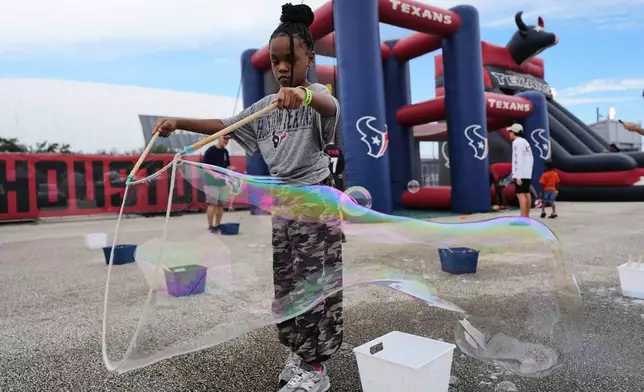 Love Womack, 7, plays with bubbles during Back Together Weekend at the Houston Texans' NFL football training camp Saturday, July 26, 2025, in Houston. (AP Photo/Ashley Landis)