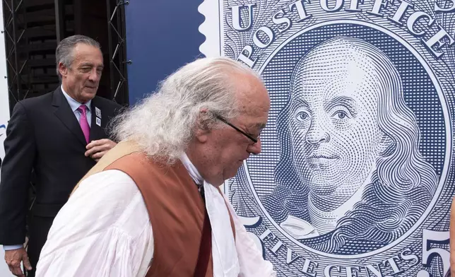 FILE - Barry Stevens, portraying Benjamin Franklin, right, walks past a just unveiled stamp marking the 250th anniversary of the postal service, Wednesday, July 23, 2025, in Washington, as Postmaster General David Steiner looks on. (AP Photo/Cliff Owen, File)