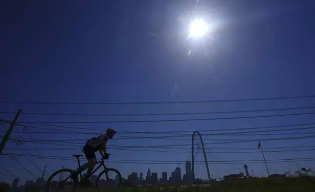 A bicyclist passes power lines near downtown Dallas, Tuesday, July 29, 2025. (AP Photo/LM Otero)