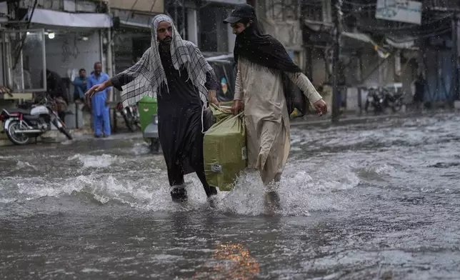 Local residents carry a big bag as they walk through a flooded road during monsoon rainfall, in Rawalpindi, Pakistan, Thursday, July 17, 2025. (AP Photo/Anjum Naveed)