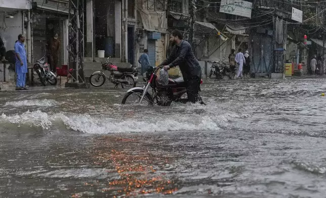 A man walks with his motorcycle through a flood road caused by heavy monsoon rains, in Rawalpindi, Pakistan, Thursday, July 17, 2025. (AP Photo/Anjum Naveed)