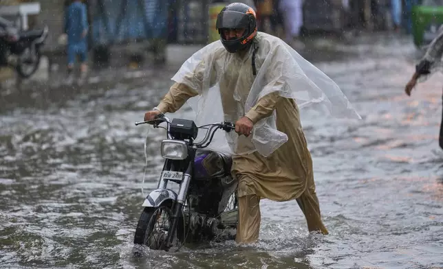 A man walks with his motorcycle through a flooded road during monsoon rainfall, in Rawalpindi, Pakistan, Thursday, July 17, 2025. (AP Photo/Anjum Naveed)