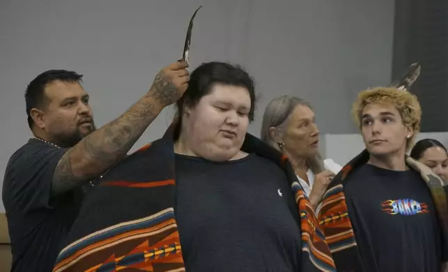 Relatives place bald eagle feathers on the heads of new high school graduates, as a mark of accomplishment and as reverence to the bird they hold sacred, at a ceremony at the Prairie Island Indian Community in Minnesota on Wednesday, July 9, 2025. (AP Photo/Giovanna Dell'Orto)