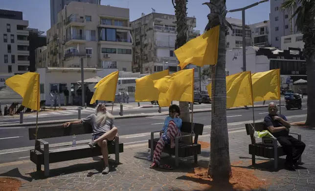 People sit on benches, decorated with yellow flags symbolizing the hostages being held by Hamas in the Gaza Strip, at the beachfront in Tel Aviv, Israel, Friday, July 4, 2025. (AP Photo/Oded Balilty)