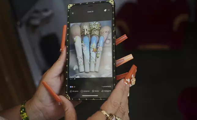 Miralys Maura Cruz, wearing long, decorative nails, shows a photo of nail designs she likes, at her home in La Gallega, Havana province, Cuba, Saturday, June 28, 2025. (AP Photo/Ramon Espinosa)