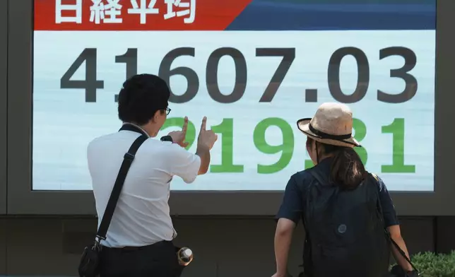 People speak in front of an electronic stock board showing Japan's Nikkei index at a securities firm Friday, July 25, 2025, in Tokyo. (AP Photo/Eugene Hoshiko)