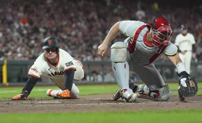 San Francisco Giants' Matt Chapman, left, slides home to score against Philadelphia Phillies catcher J.T. Realmuto during the eighth inning of a baseball game in San Francisco, Monday, July 7, 2025. (AP Photo/Jeff Chiu)