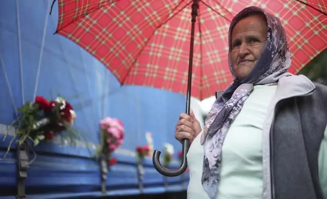 A woman stands next to a truck carrying remains of the identified victims of the 1995 Srebrenica massacre to the Memorial centre in Potocari, where they will be buried on July 11, in Visoko, Bosnia, Wednesday, July 9, 2025. (AP Photo/Armin Durgut)