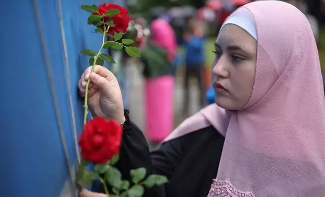 A woman places a flower on a truck carrying remains of the identified victims of the 1995 Srebrenica massacre to the Memorial centre in Potocari, where they will be buried on July 11, in Visoko, Bosnia, Wednesday, July 9, 2025. (AP Photo/Armin Durgut)